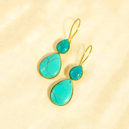 Elegant brass dangle earring with a teardrop shape, adorned with a large turquoise-colored gemstone displaying natural black veining at the bottom. A smaller sea-green turquoise stone sits at the top, secured with a classic curved hook