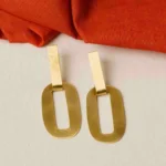 Modern brass drop earring with a sculptural design, showcasing an oval-shaped top with a hollow center, two i+CF300nterlinked hoops, and a textured triangle charm gracefully dangling at the bottom, secured with a push-back closure