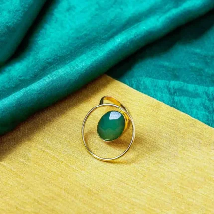 Modern geometric ring with a polished gold-tone finish also a round wire structure, and a emerald-green stone in the middle