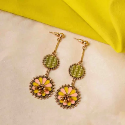 Statement metal drop earrings with an oxidized gold-tone finish, colored top disc, floral-patterned bottom disc, peach and yellow enamel detailing, and a push-back closure