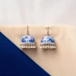 Elegant silver-finish jhumka earring with butterfly meenakari artwork, a detailed circular top, pearl bead accents, and a secure push-back closure.