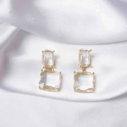 Sleek gold-tone dangle earrings with two slinging rectangular clear crystals, each with a soft golden hue, fastened with a push back post