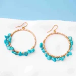 Chic metal hoop earrings featuring a polished gold-tone finish, playful turquoise beaded accents, and a curved hook back for easy wear.