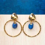 Chic metal hoop earrings featuring a polished gold-tone finish, dangling blue assymetrical stone, a golden charm and, a push back for easy wear.