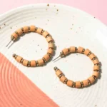 Chic metal hoop earrings featuring a polished gold-tone pearls, with peach coloured wooden beads along with small circular golden beads a push back for easy wear.