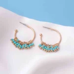 Chic metal hoop earrings featuring a polished gold-tone finish,/turquoise finish featuring dangling turquoise coloured mini beads at the curve , and a push back for easy wear