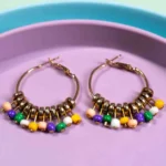 Chic metal hoop earrings featuring a polished gold-tone finish, multicolor finish featuring circular shaped golden beads, coloiurful dangling beads at the bottom and a hinged back.