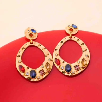 Unique gold-tone drop earrings featuring irregular hammered circular discs, shimmering clear and colorful gemstone embellishments, and a secure push-back closure .