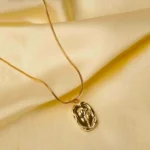 Sophisticated gold-tone snake chain necklace with a slightly irregular framed oval pendant, adorned with an embossed flower motif, complete with a lobster claw closure.