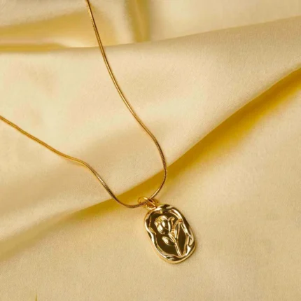 Sophisticated gold-tone snake chain necklace with a slightly irregular framed oval pendant, adorned with an embossed flower motif, complete with a lobster claw closure.