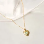 Stylish gold-tone necklace with a filled flat cable chain, an elegant heart pendant,with delicate filigree and a light opal blue stone in the center and a lobster claw clasp.