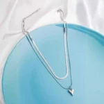 Modern two layered snake chain necklace with a polished silver finish, a solid heart charm, and an adjustable lobster clasp.