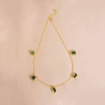 Sophisticated polished gold-tone curb chain necklace featuring shimmering emerald-green raw gemstones set in irregular teardrop designs, complete with an S-hook clasp.