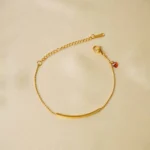 Minimalist gold-tone bracelet with a fine satellite chain, a sleek curved rectangular bar, and a petite orange heart charm, finished with a secure lobster claw clasp.