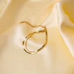 Elegant adjustable curb chain bracelet in a gold-tone finish, featuring a curved metallic wire centerpiece with a dangling spherical charm and a secure spring ring clasp.