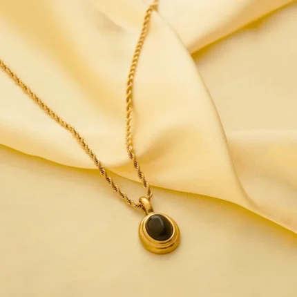 Refined rope chain necklace in a gold-tone finish, showcasing an oval pendant with a textured gezel pattern and a deep black gemstone centerpiece, lobster clasp closure.