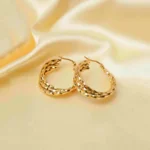 Refined and unique twisted spiral hoop earrings with three interwoven metal strands, a gleaming gold-tone finish, and a hinged back for easy wear.