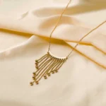 Stylish gold-tone necklace with a filled flat cable chain, an elegant crescent pendant, and fine dangling chains ending in circular golden beads