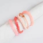 Pack of five pink and coral beaded stretch bracelets, one with a heart charm and one with a gold chain
