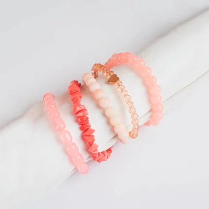Pack of five pink and coral beaded stretch bracelets, one with a heart charm and one with a gold chain