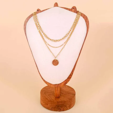 A pre-layered gold-toned necklace featuring three connected chains of varying lengths and textures, with a large, polished circular coin or medallion pendant hanging from the longest chain.