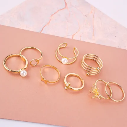 "Eight gold-toned fashion rings with artificial pearls, featuring coils, flowers, open-ended designs, and stacking bands. Perfect for versatile, trendy looks."