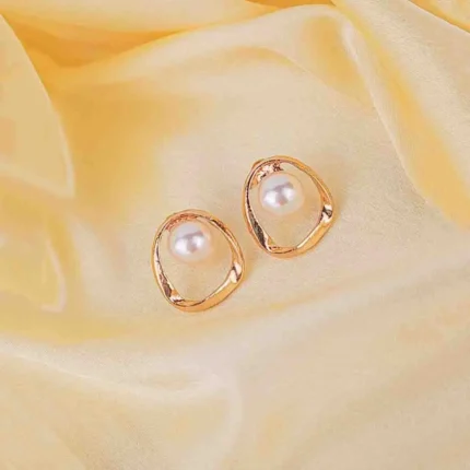 A single gold-toned earring featuring a large, luminous white faux pearl suspended within an open, asymmetrical, swirling gold-toned orbit frame.