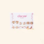 A collection of seven pairs of small, gold-toned stud earrings displayed on a card. The eclectic designs include polished gold spheres, a butterfly, a cloud, musical notes, a heart, and two different styles of airplane studs.