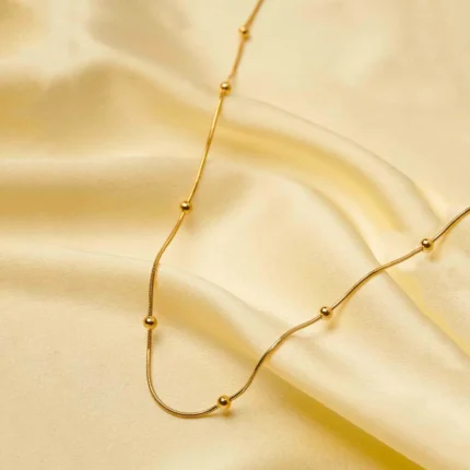 Minimalist gold-tone bracelet with a fine satellite chain, a sleek curved rectangular bar, and a petite orange heart charm, finished with a secure lobster claw clasp.