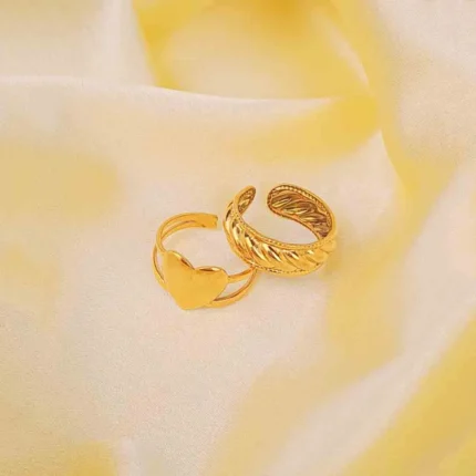 A pair of adjustable gold-toned rings: one is a thick braided or croissant style, and the other is a thin stack ring with a heart shape.