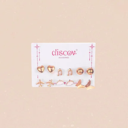A collection of seven pairs of small, gold-toned stud earrings displayed on a card. The eclectic designs include polished gold spheres, a butterfly, a cloud, musical notes, a heart, and two different styles of airplane studs.