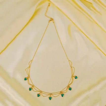 Layered gold necklace with emerald green heart charms and lobster clasp.