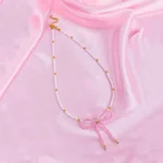 White and gold beaded necklace with a pink pearl bow pendant and gold adjustable clasp, styled for a modern, feminine look.