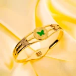 Gold bracelet with a green butterfly at the center, polished finish, and adjustable closure for a stylish and elegant look.
