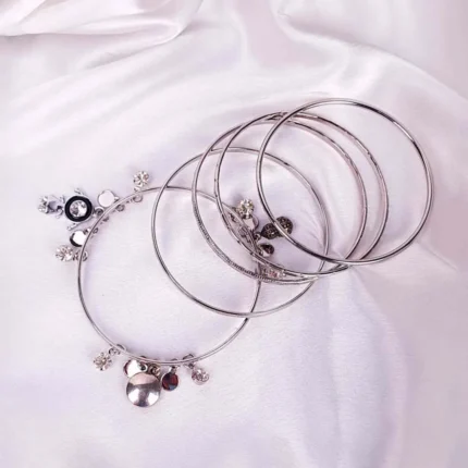 Set of five polished silver bangles, one styled with hanging charms and sleek finish, ideal for trendy stacked look.