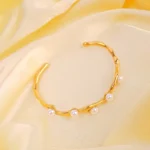 Gold wavy open cuff bracelet with faux pearl accents and glossy finish