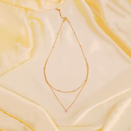 Gold layered necklace with bead accents, crystal charm, and adjustable lobster clasp.