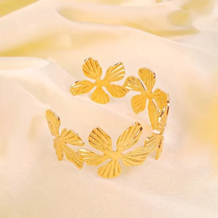 a wide, gold-colored open-cuff bracelet decorated with an array of individual flower motifs