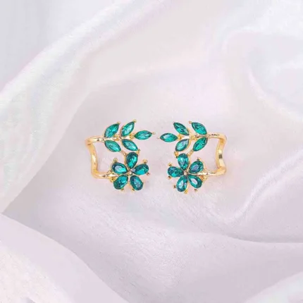 Ear cuffs with floral and leaf motif, emerald-toned crystals, polished metal, and secure push-back closure.