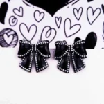 Elegant black bow-shaped earrings outlined with white pearls and featuring a secure push-back closure.
